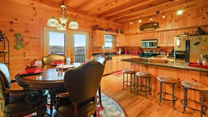 A wooden cabin interior with a dining area, kitchen, and bar stools. - Family Cabin With Mountain Views (Boone)