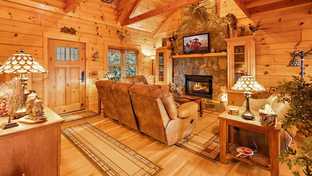 A cozy log cabin interior with a stone fireplace, wooden furniture, and a television mounted above it. - Family Cabin With Mountain Views (Boone)