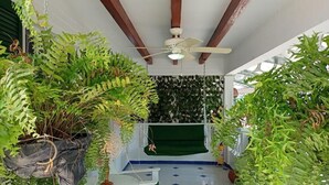 Un espacio exterior techado con ventilador de techo, plantas colgantes y piso de baldosas.