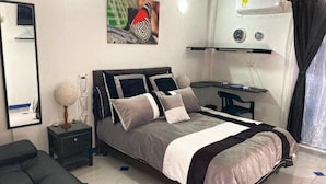 Un dormitorio con cama, mesitas de noche, una silla, un escritorio y un aire acondicionado de pared.