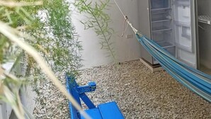 Una habitación con una hamaca, un refrigerador y ventana con vistas a un jardín.