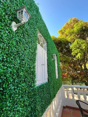 A building with a green ivy-covered exterior, a white door, and a small window with a white frame. - Hostal Paraiso Minca (Santa Marta)