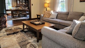 Una sala de estar con sofá, mesa de centro y televisor. Se ve, a través de un arco, un comedor con mesa y sillas.
