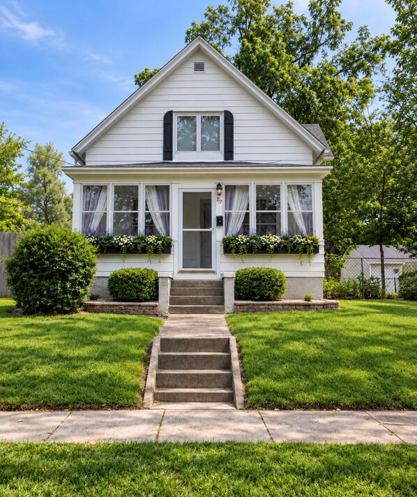 A two-story house with a front porch, a set of stairs leading to the entrance, and a well-maintained lawn.
