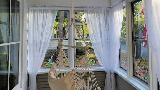 Una habitación con una silla colgante, ventanas amplias con cortinas blancas y un ventilador de techo.
