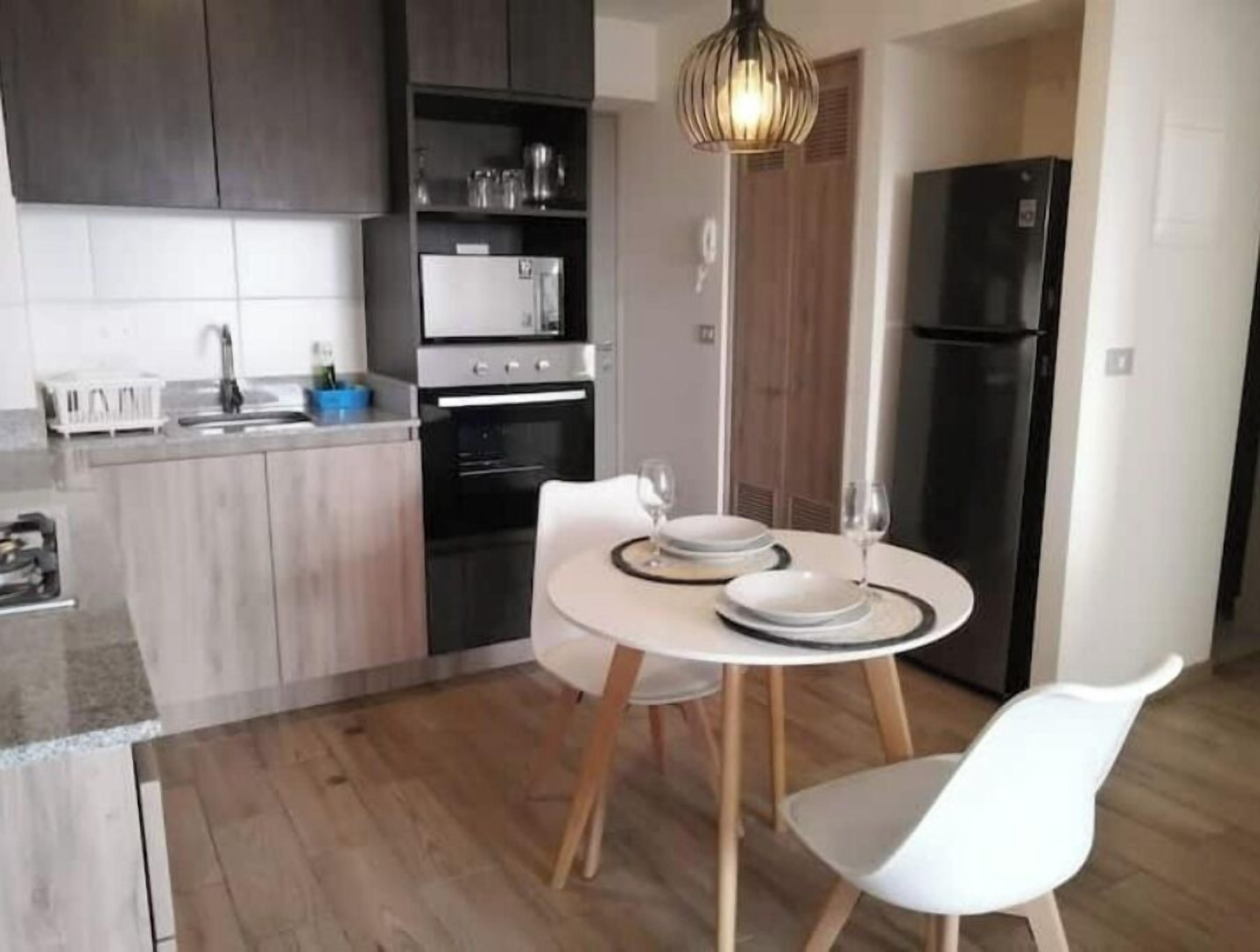 A modern kitchen with a dining area, featuring a central island, a built-in oven, and a refrigerator.