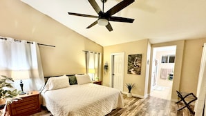 A bedroom with a bed, a nightstand, a lamp, a ceiling fan, a door, and a window. - PC Furn Golf Course Home. 36 PB courts for Nat's Nov `24 incl cart, hk 'ing util (Goodyear)