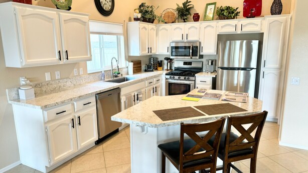 A modern kitchen with white cabinetry, a central island, stainless steel appliances, and decorative plants. - PC Furn Golf Course Home. 36 PB courts for Nat's Nov `24 incl cart, hk 'ing util (Goodyear)