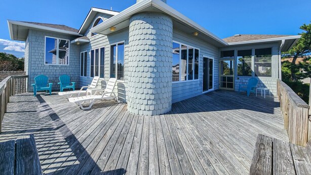 A coastal house with a wooden deck, a large chimney, and a covered patio area with chairs. - PLEASURE ISLAND - 5 BR Home in Schooner Ridge w/Access to Community Pools & Rec Center (Duck)