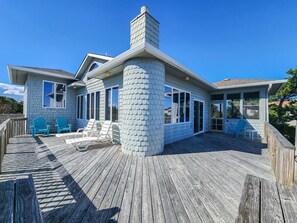 A coastal house with a wooden deck, a large chimney, and a covered patio area with chairs. - PLEASURE ISLAND - 5 BR Home in Schooner Ridge w/Access to Community Pools & Rec Center (Duck)