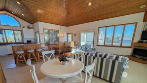 A spacious living area with a round table and chairs, a striped sofa, and a kitchen area with wooden cabinets and a large window. - PLEASURE ISLAND - 5 BR Home in Schooner Ridge w/Access to Community Pools & Rec Center (Duck)