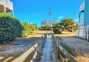 Un sendero que conduce a una casa con terraza de madera y aro de baloncesto.