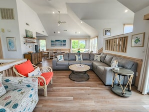 A spacious living room with a large gray sectional sofa, a round coffee table, and a wicker chair with red cushions.