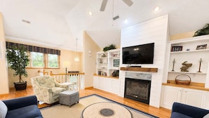 A living room with a fireplace, a television, and a large window. - Driftin South - 5 BR Oceanside Home in Duck - Short Walk to Shops & Restaurants (Duck)