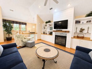 A living room with a fireplace, a television, and a large window. - Driftin South - 5 BR Oceanside Home in Duck - Short Walk to Shops & Restaurants (Duck)