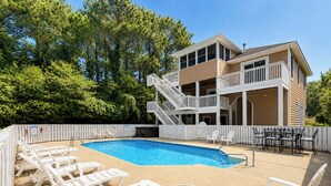 A pool area with lounge chairs and a building with a balcony. - Driftin South - 5 BR Oceanside Home in Duck - Short Walk to Shops & Restaurants (Duck)