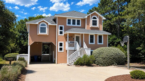 A two-story house with a covered porch, a front entrance, and a basketball hoop. - Driftin South - 5 BR Oceanside Home in Duck - Short Walk to Shops & Restaurants (Duck)