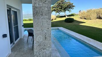A pool area with a stone column, a chair, and a view of a tree and landscape.