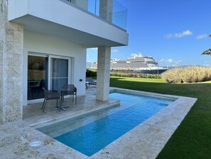 A modern outdoor pool area with a glass door leading to a seating area, a large cruise ship in the background, and a well-maintained lawn. - VIP Resort all inclusive 5 Star Resort steps from the beach with Premium rooms (Puerto Plata)