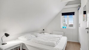 Et soveværelse med seng, skrivebord, lampe, et vindue og en radiator.