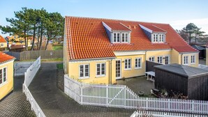 En gul bygning med rødt tegltag, hvide vinduer og et hvidt stakittancehegn.