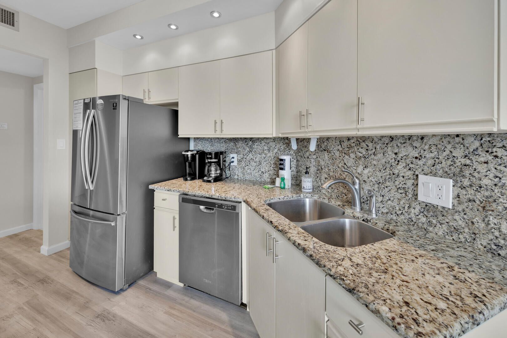 Eine moderne Küche mit Edelstahl-Kühlschrank, Geschirrspüler, einer Arbeitsplatte aus Granit und weißen Schränken.