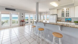 A kitchen with a view of the ocean, white cabinets, and a bar area with stools. - Hobbs Realty - Enjoy "Miss B Haven", a pet-friendly oceanfront home w/ private pool (Holden Beach)