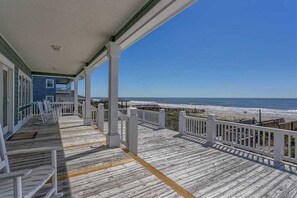 A wooden deck with white railings overlooking a beach.