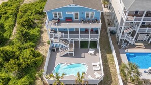 A two-story house with a swimming pool, a deck, and a view of the beach.