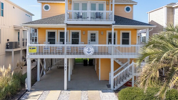 A two-story yellow building with a balcony, a sign for 'HBS Realty', and a 'LEGACY' logo. - Legacy - A beautiful 4-bedroom home with a community dock, minutes from the ocean. (Holden Beach)
