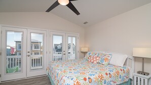 A bedroom with a bed, two bedside tables, a ceiling fan, and a view through the doors. - Legacy - A beautiful 4-bedroom home with a community dock, minutes from the ocean. (Holden Beach)