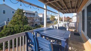 A covered outdoor patio with a table and chairs, overlooking a residential area with houses and a tree. - Legacy - A beautiful 4-bedroom home with a community dock, minutes from the ocean. (Holden Beach)