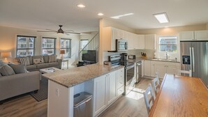 A modern kitchen with white cabinets, stainless steel appliances, and a wooden dining table. - Legacy - A beautiful 4-bedroom home with a community dock, minutes from the ocean. (Holden Beach)