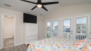 A bedroom with a bed, a ceiling fan, a TV, and a view of the outside. - Legacy - A beautiful 4-bedroom home with a community dock, minutes from the ocean. (Holden Beach)