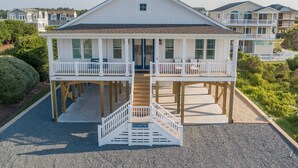 A two-story house with a balcony on the upper floor, a front porch, and a staircase leading to the entrance. - Hobbs Realty - Spend many an “Oh Happy Day” when you enjoy this charming home with a pool. (Holden Beach)