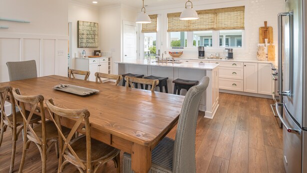 A spacious kitchen with a wooden dining table, white cabinetry, and a large island. - Hobbs Realty - Spend many an “Oh Happy Day” when you enjoy this charming home with a pool. (Holden Beach)