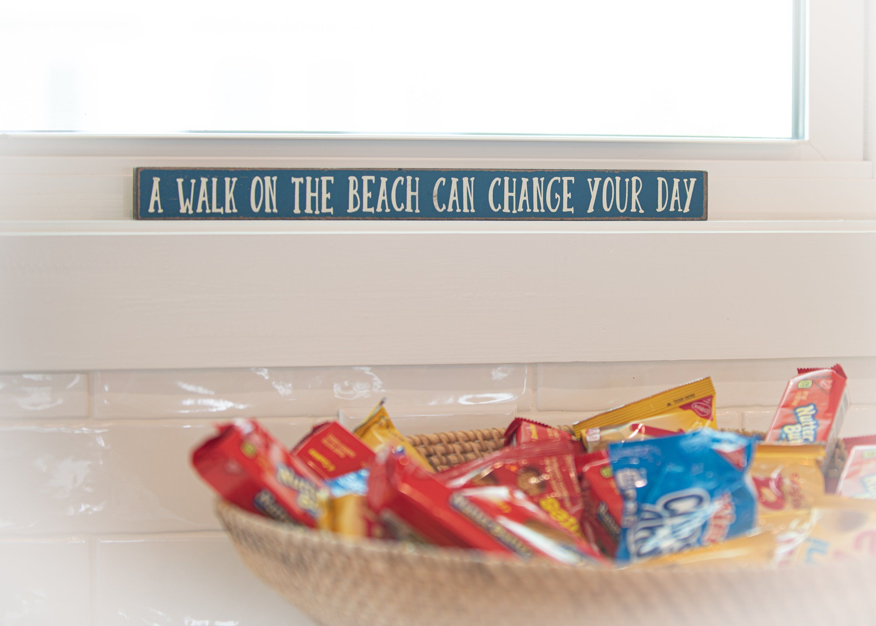 Un cartel con la frase: 'Un paseo por la playa puede cambiar tu día', sobre una cesta llena de diversos aperitivos.