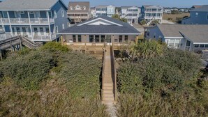 A coastal house with a wooden deck leading to a front porch, surrounded by dense shrubbery. - See why this is “Our Happy Place” in this pet-friendly, oceanfront home with a hot tub. (Holden Beach)