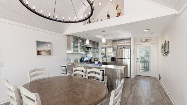 A modern kitchen with stainless steel appliances, a dining area with a round table and white chairs, and a ceiling with a circular light fixture. - See why this is “Our Happy Place” in this pet-friendly, oceanfront home with a hot tub. (Holden Beach)