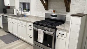 Une cuisine moderne avec des meubles blancs, une cuisinière en acier inoxydable et une hotte en bois au-dessus du four.