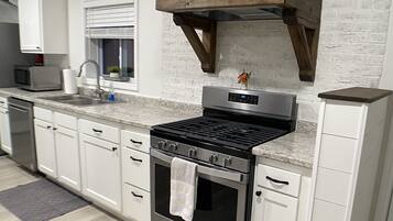 Una cucina moderna con mobili bianchi, un fornello in acciaio inossidabile e una cappa di legno sopra il forno.
