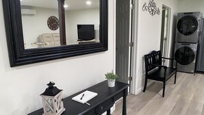 Un salon moderne avec un grand miroir, une console noire ornée d’une plante et une cuisinière à deux brûleurs.
