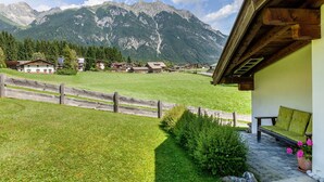 Paesaggio montano con case, una recinzione di legno e una panchina fiorita.