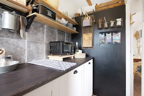 Eine Küche mit Mikrowelle, Holzregalen und einer dunklen Wand mit hängenden Gegenständen.