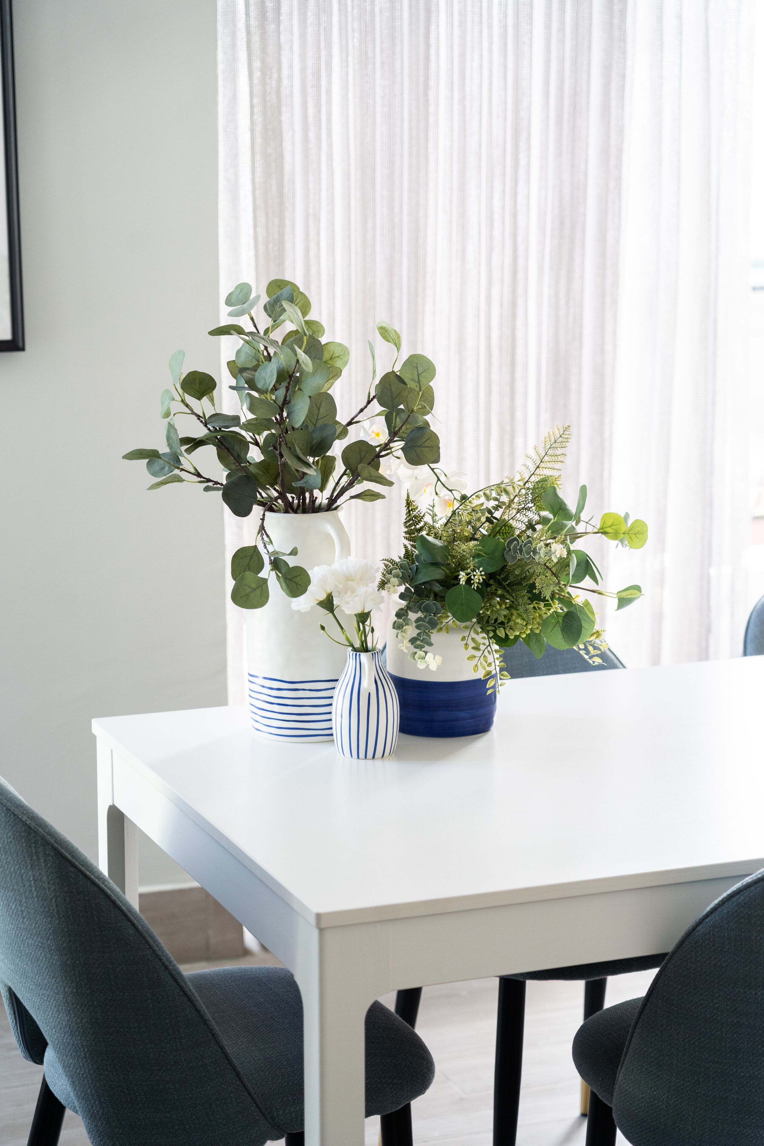 A dining table with two potted plants, a white vase, and a striped vase.