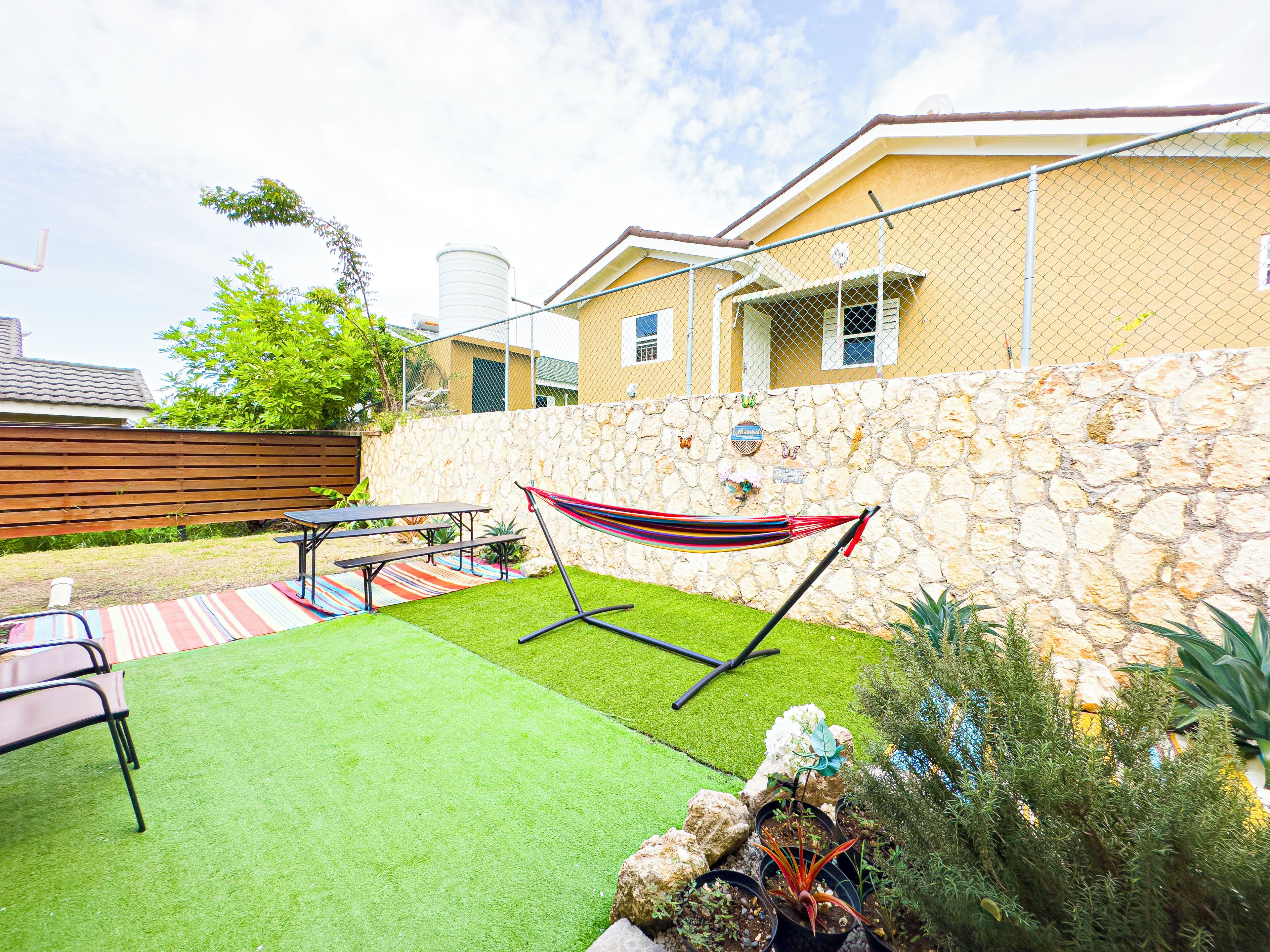 A backyard with artificial grass, a hammock, a picnic table, and potted plants.