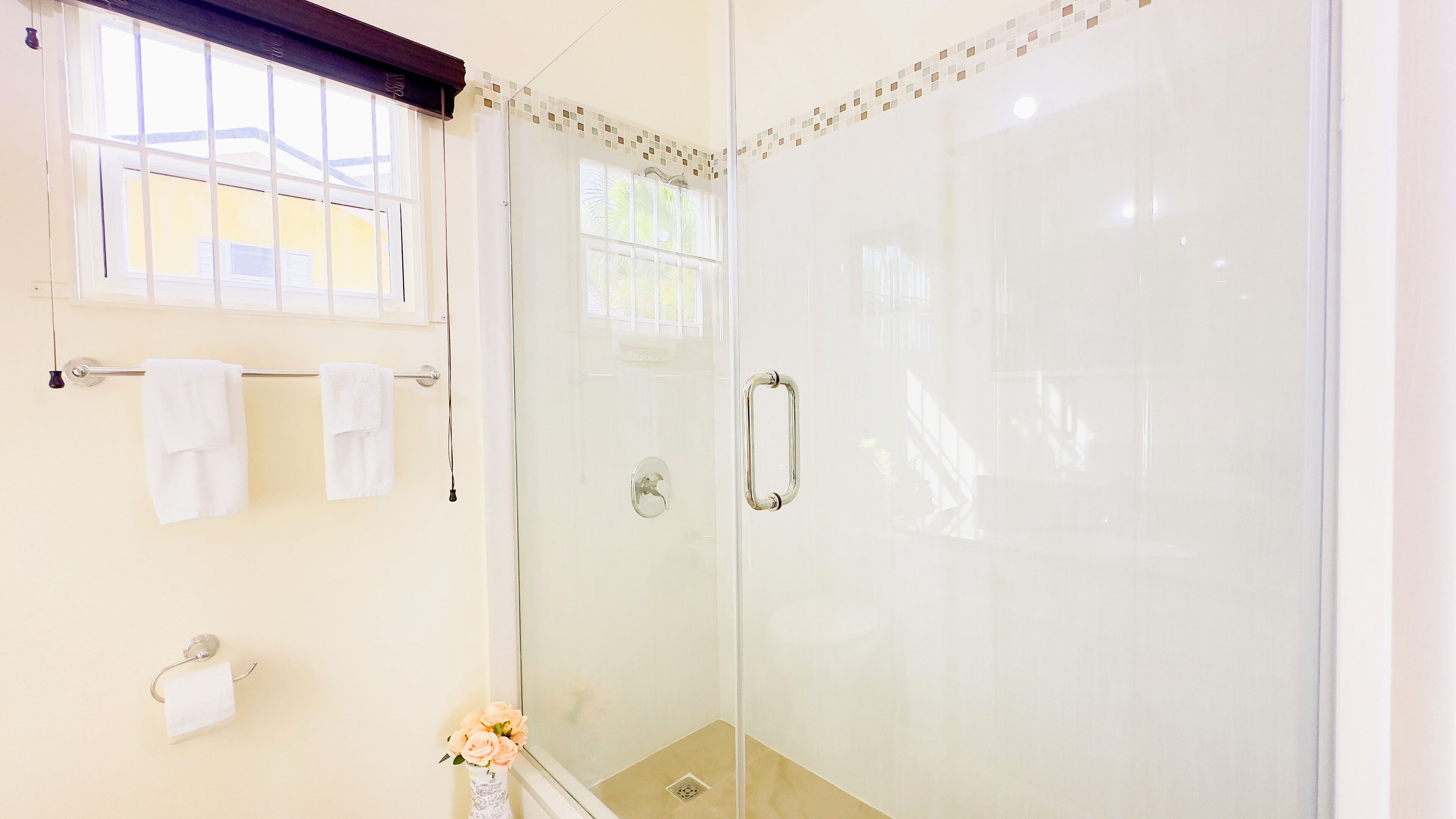 Un bagno moderno con cabina doccia in vetro, un portasciugamani con asciugamani bianchi e un vaso con fiori sulla parete.