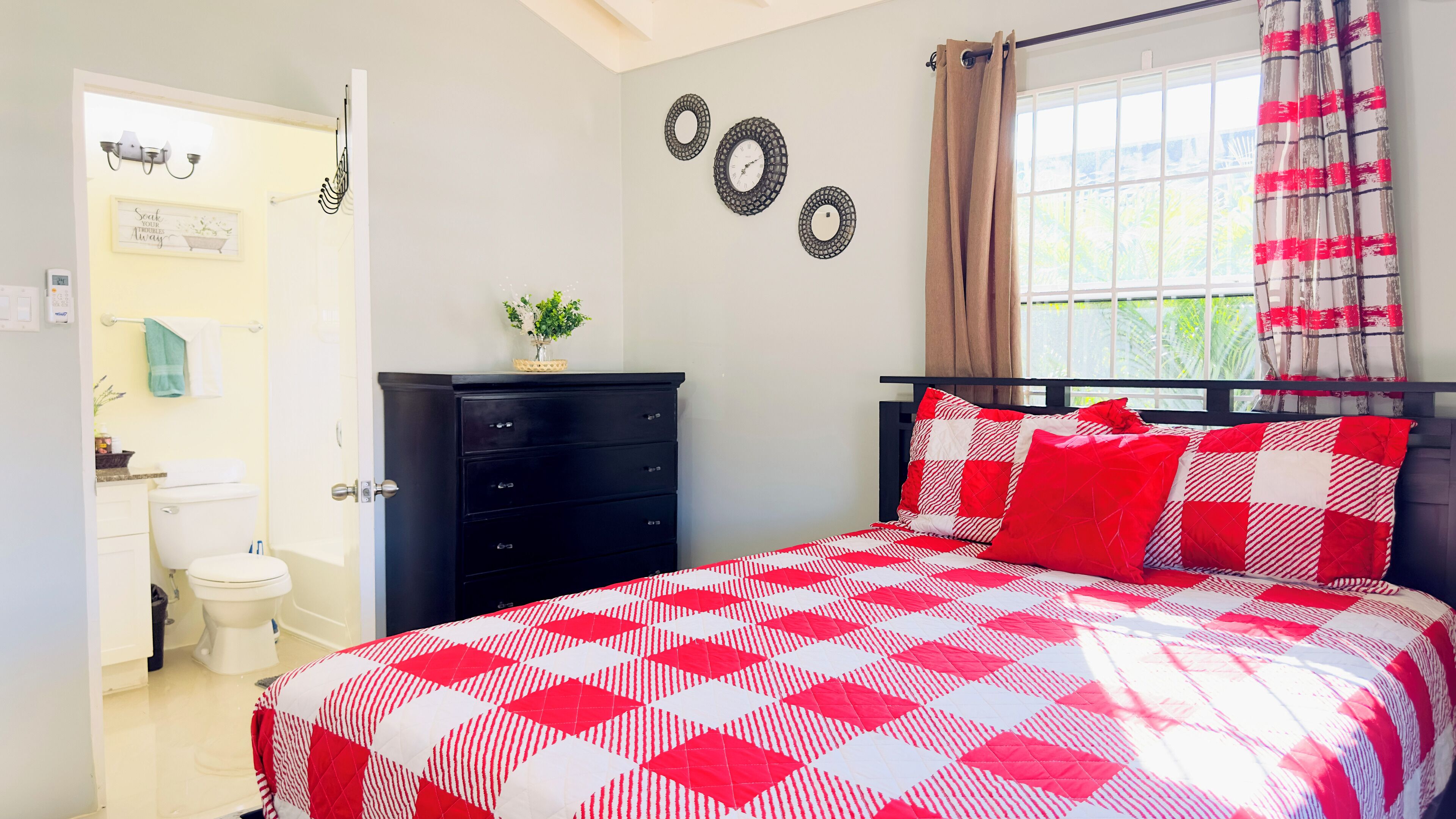 A bedroom with a bed, a dresser, a window with curtains, and a wall with decorative items.