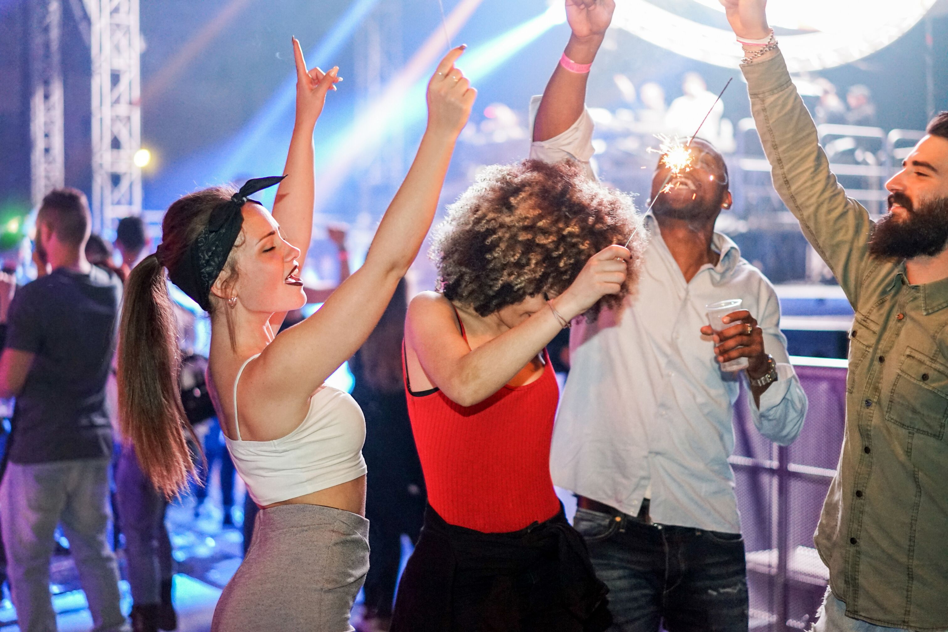 A group of people dancing at a concert with stage lighting in the background.