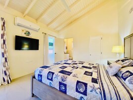 A bedroom with a bed, a TV, an air conditioner, and a bathroom visible through an open door.